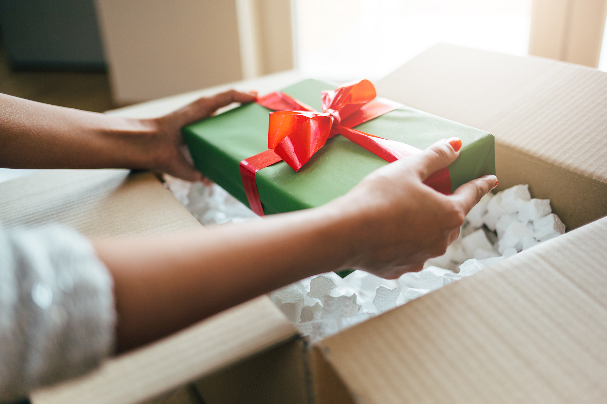 A gift wrapped in green wrapper and has a red bow tie being taken out of a bigger box